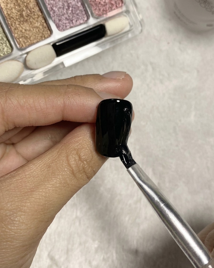 Un pincel de punta dividida trazando líneas verticales texturizadas con pegamento transparente sobre la superficie de una uña de gel negro.