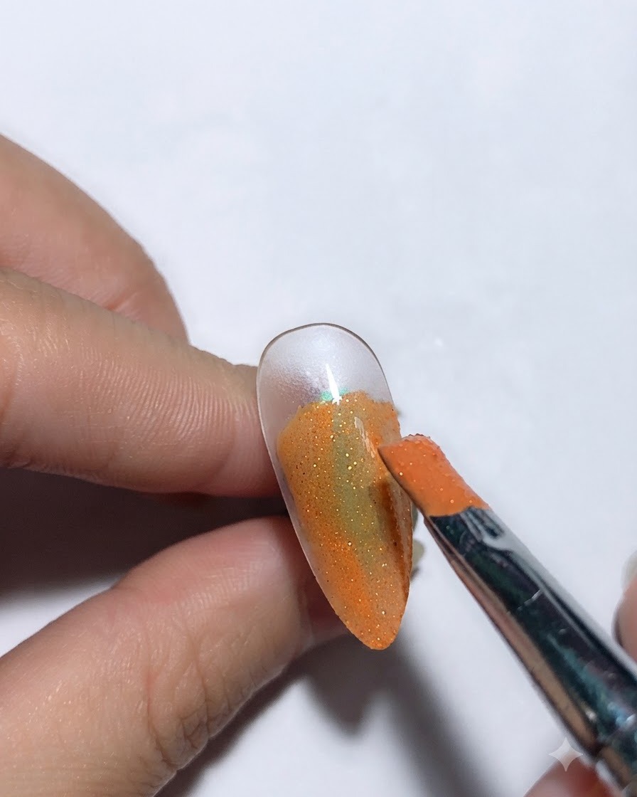 Un pincel aplicando pegamento para cielo estrellado sobre una base de uña de color naranja.