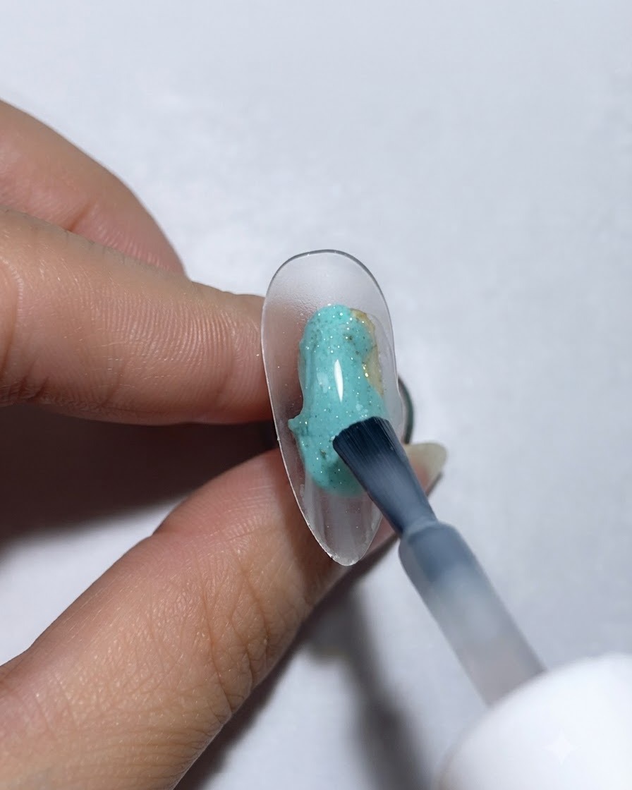 Un pincel aplicando base de gel proteico sobre una uña transparente de exhibición.