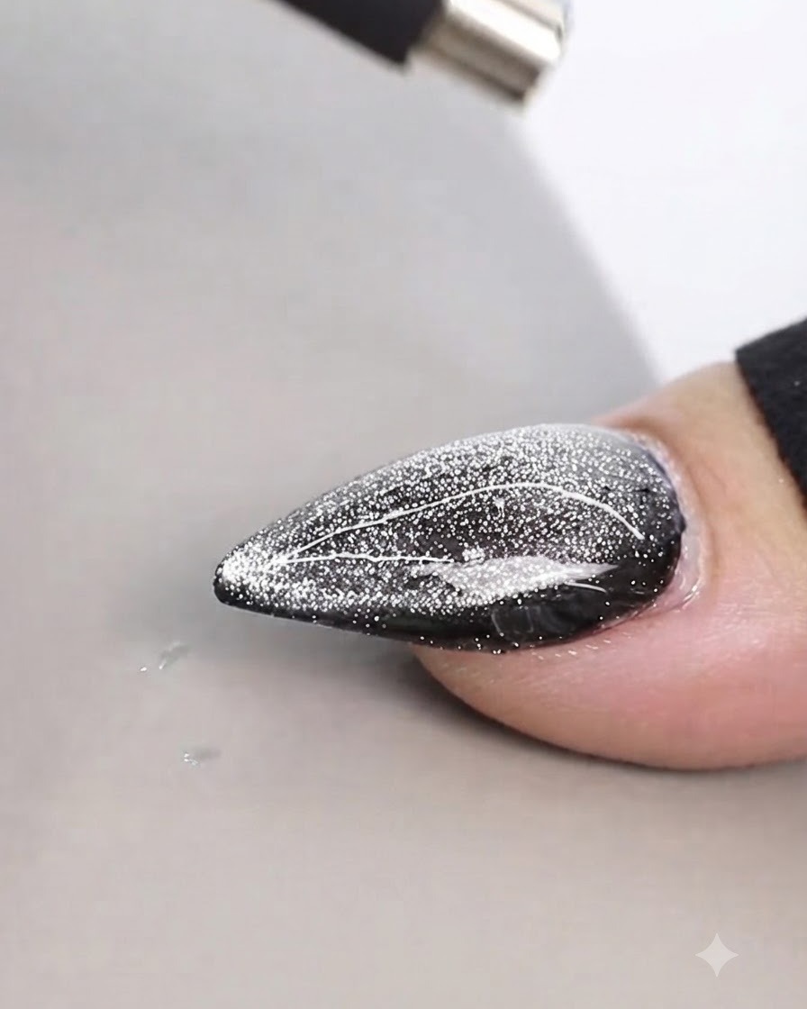 Un imán cilíndrico sostenido muy cerca por encima de un diseño de uña cat eye brillante para crear líneas finas.