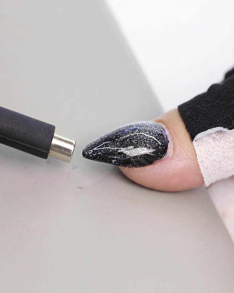 Una herramienta magnética estilo bolígrafo negro acercándose a una superficie texturizada de uña cat eye.