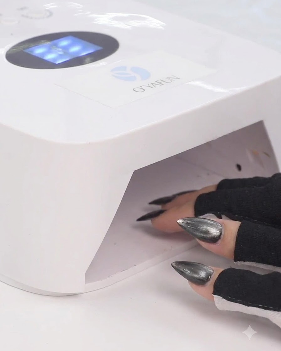 Una mano con guantes negros sin dedos colocando los dedos dentro de una lámpara de uñas LED UV blanca para curar el esmalte de gel.