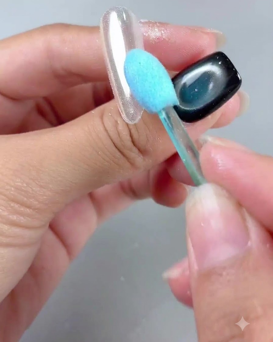 Un cepillo de mango azul limpiando suavemente el polvo de una uña con acabado de espejo brillante.