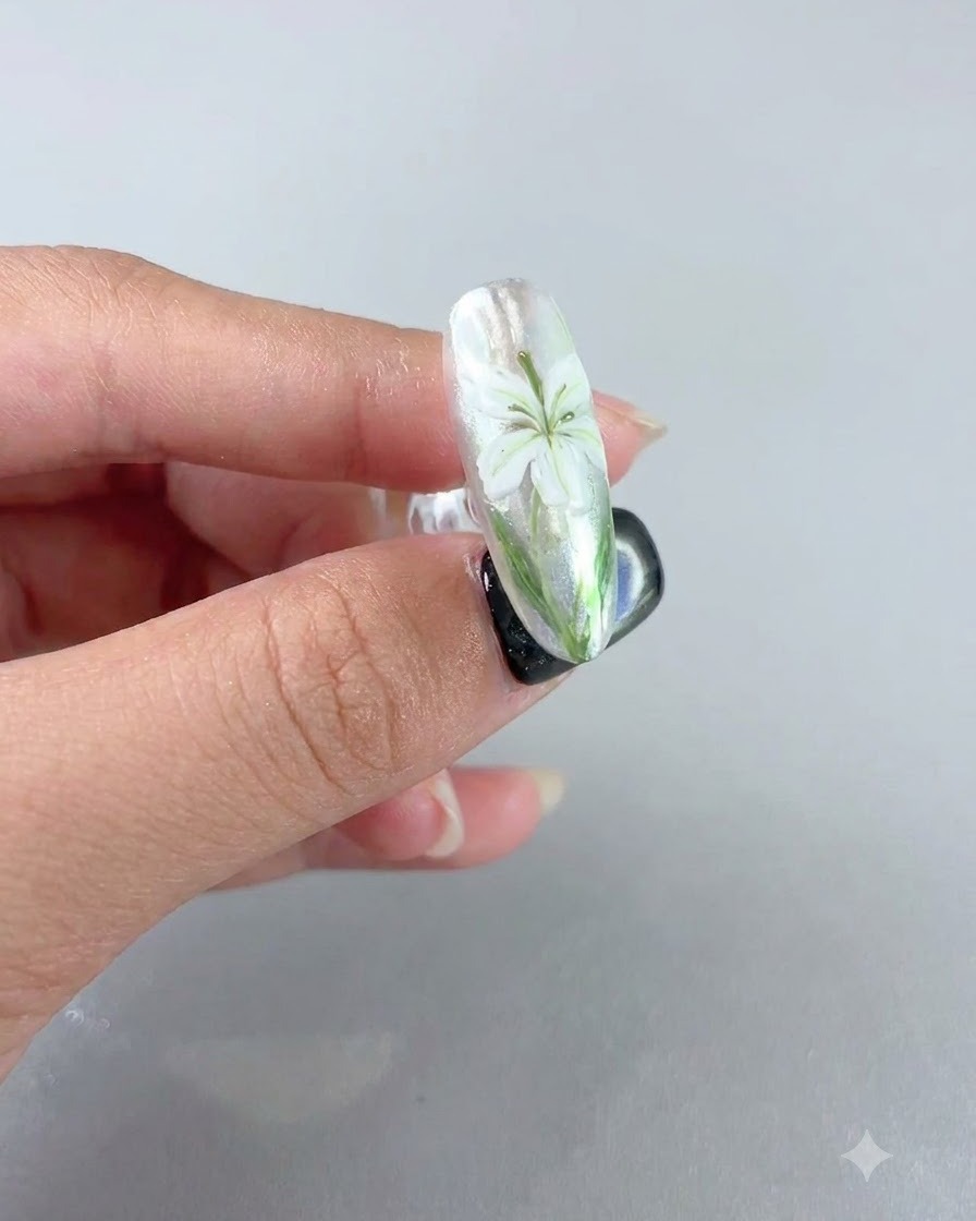 Una uña terminada que muestra el diseño de un lirio blanco bajo un acabado mate aterciopelado.