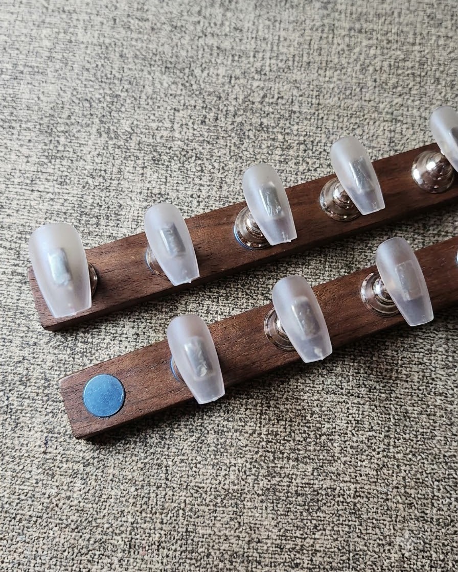 Una toallita sin pelusa limpiando el polvo de los tips de uñas transparentes colocados en un soporte de madera.