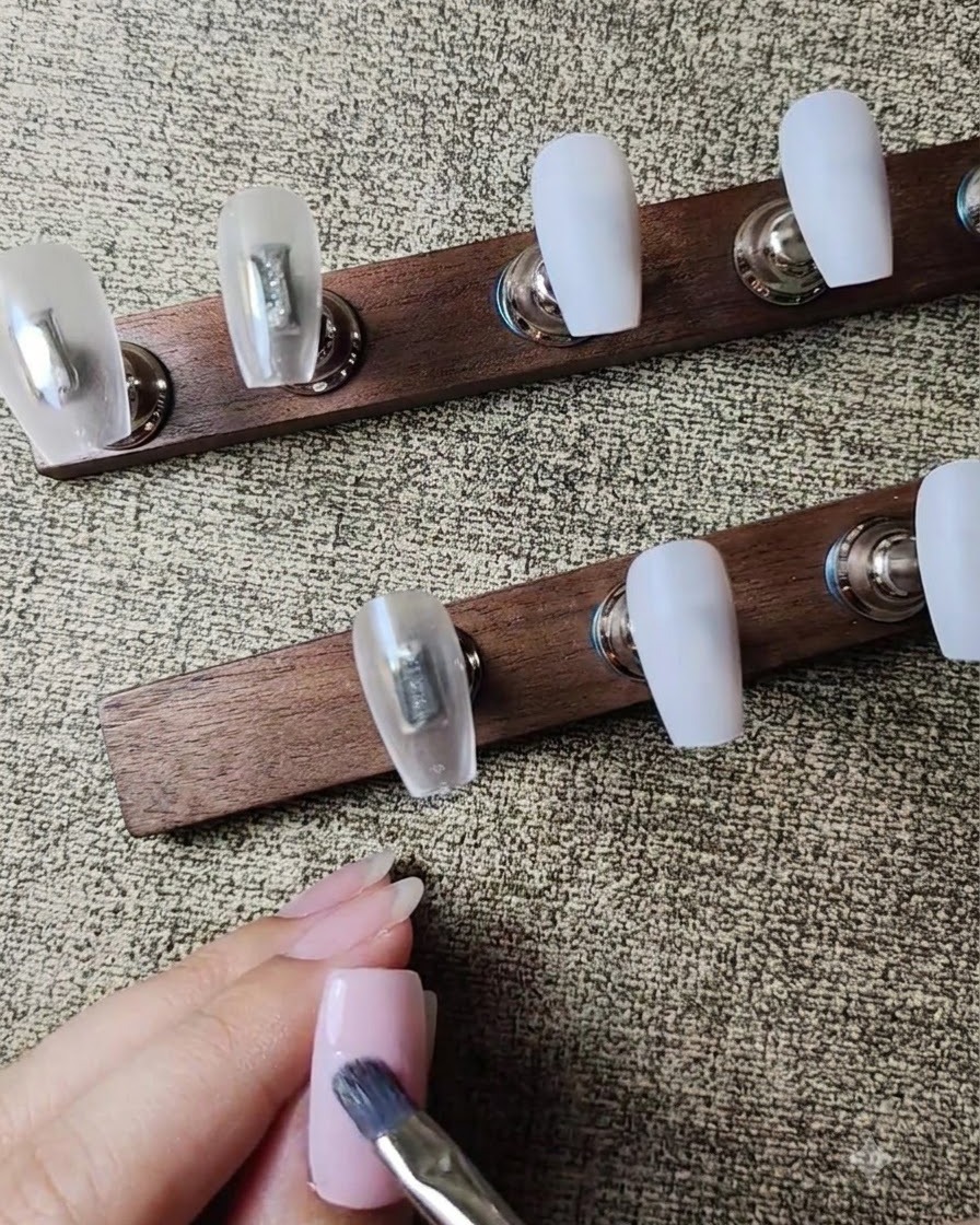 Un pincel plano aplicando una segunda capa de esmalte en gel rosa nude a la uña.
