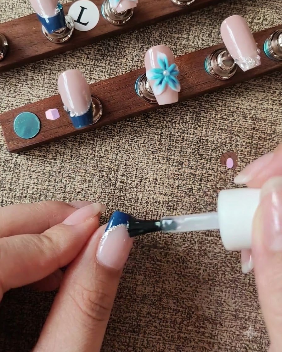 Un pincel aplicando top coat sobre la superficie de la uña mientras rodea un acento floral 3D.