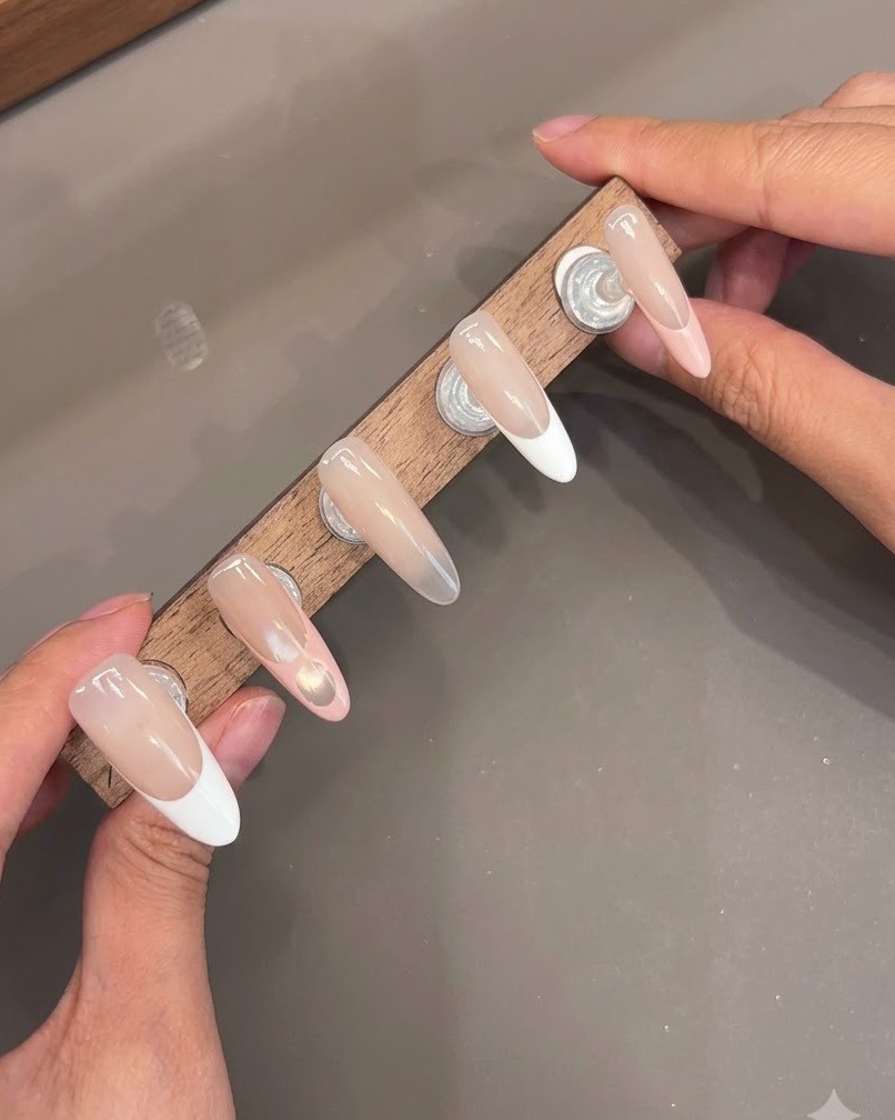 Múltiples uñas postizas montadas en un soporte de madera que muestran capas brillantes de capa superior.