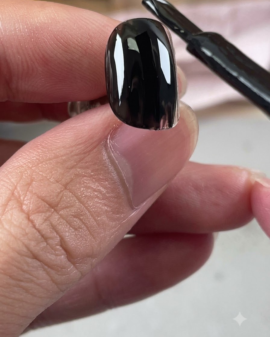 Pincel de esmalte de gel aplicando una capa brillante de base negra sobre una uña.