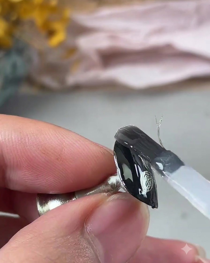 Pincel aplicando una capa de gel transparente de refuerzo sobre el diseño metálico.