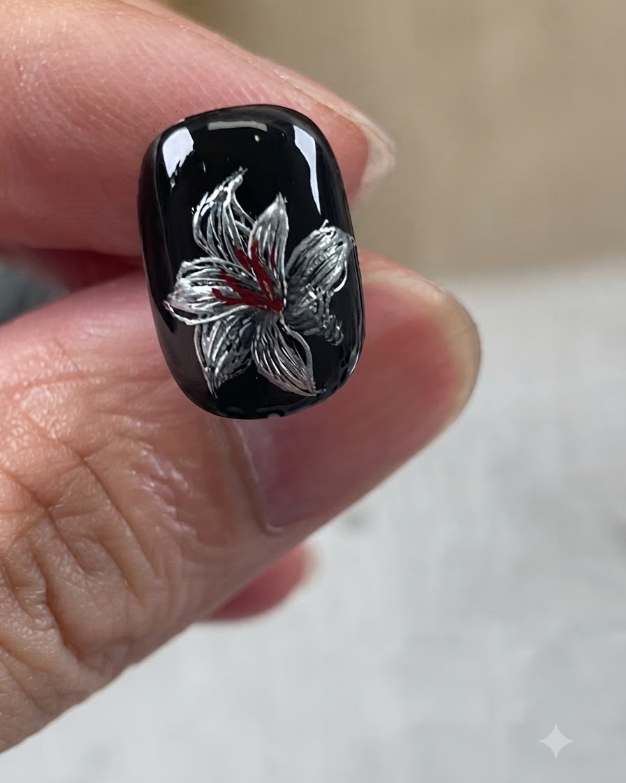 Diseño de lirio plateado terminado sobre base negra, con toques blancos y un centro rojo.