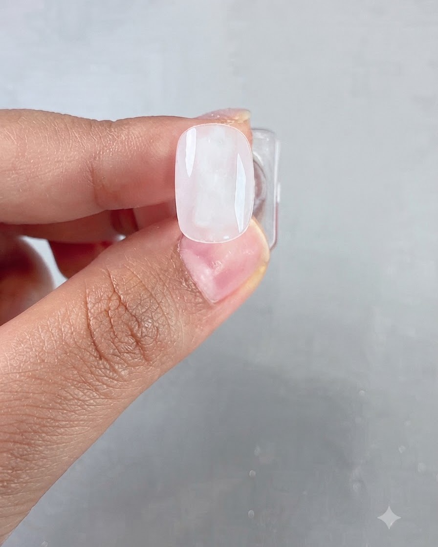 Un primer plano de un pincel aplicando una capa de gel transparente y brillante sobre una uña con base de color blanco lechoso.