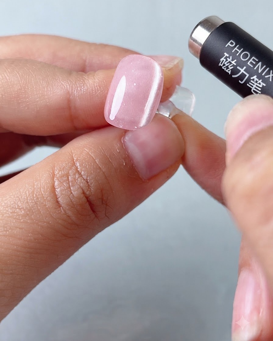 Una herramienta de lápiz magnético flotando sobre una uña de gel con efecto ojo de gato rosa para dar forma a la banda de luz.
