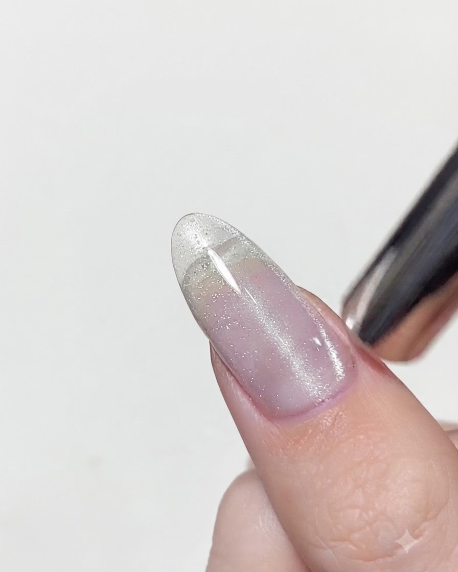 Una herramienta magnética colocada muy cerca de una uña con esmalte en gel húmedo de ojo de gato para concentrar el brillo plateado en una línea vertical.