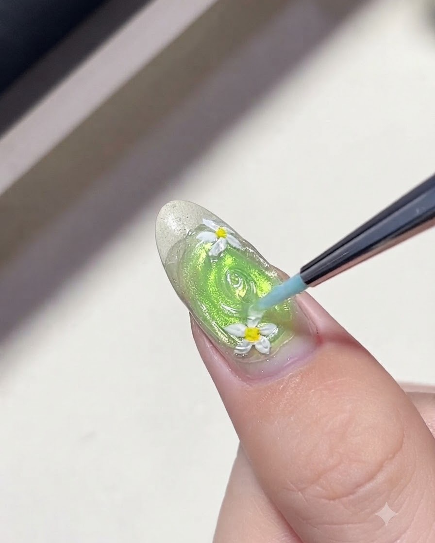 Un pincel delineador fino dibujando anillos concéntricos de gel transparente alrededor de las flores de margarita en una uña verde para crear ondas de agua.