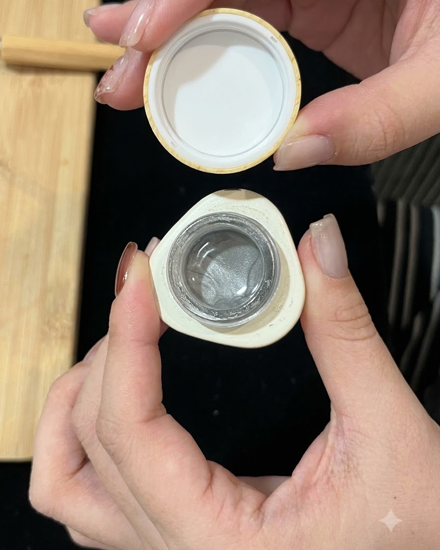Un pequeño envase de gel magnético de ojo de gato plateado abierto, mostrando la fórmula brillante en su interior.