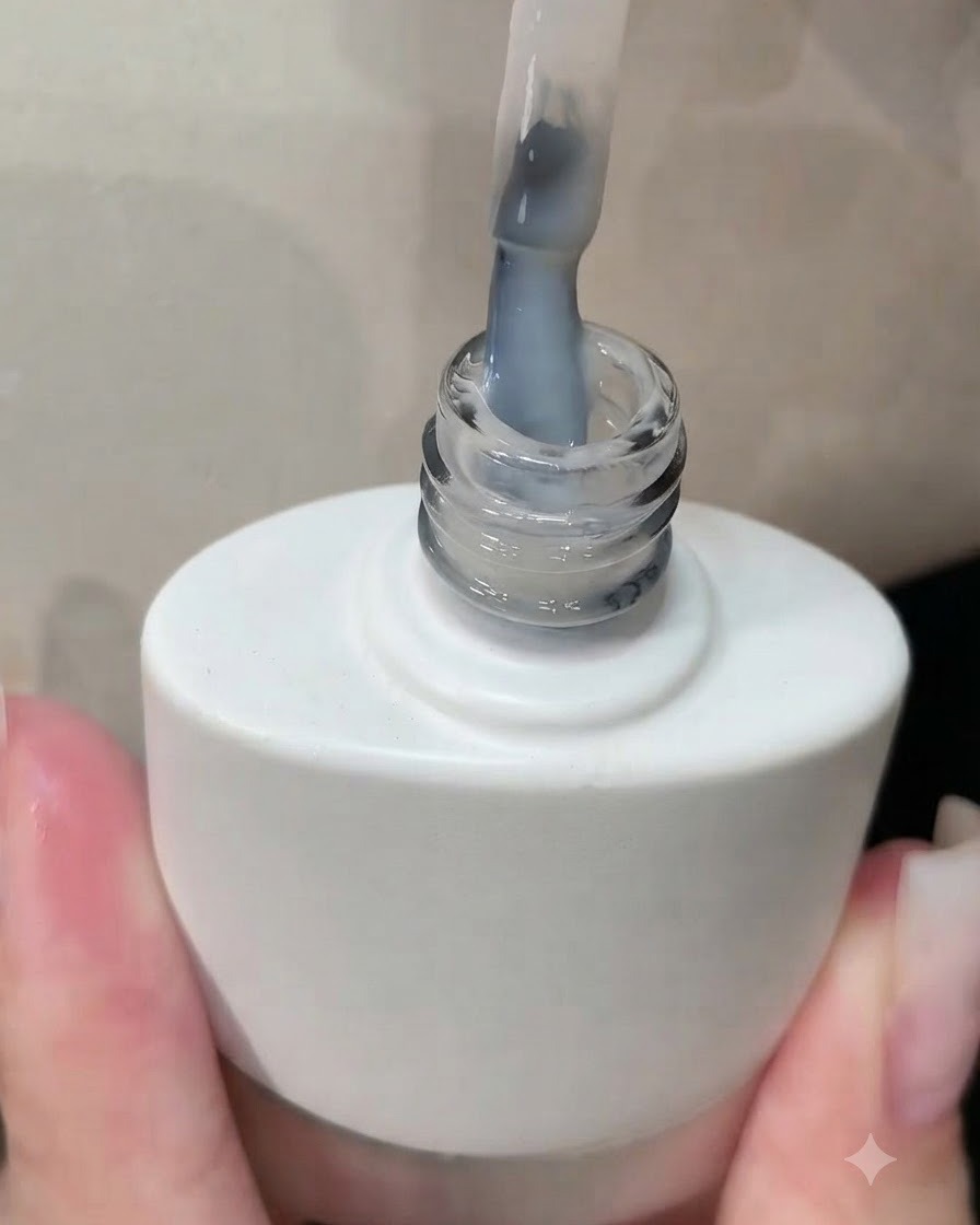 Un pincel saliendo de un frasco de esmalte de gel blanco con una capa blanca lechosa visible en las cerdas.