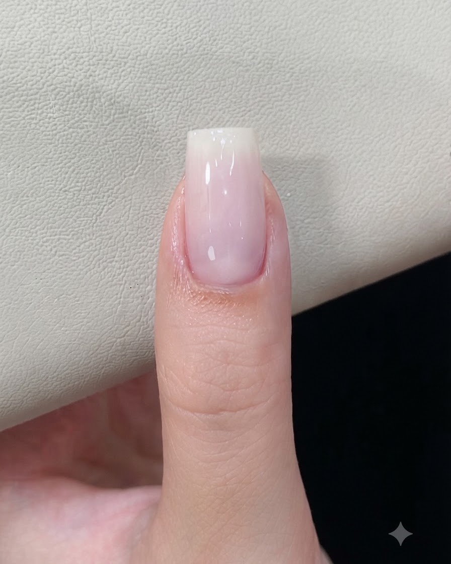 Una uña con una base de gel blanco lechoso curada reposando bajo una lámpara de uñas.
