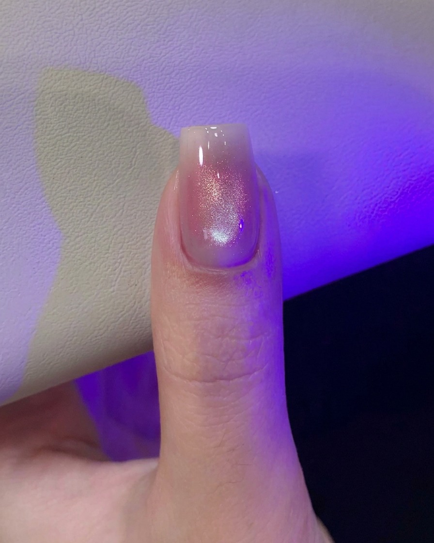 Un pulgar bajo la luz púrpura de una lámpara UV/LED curando el diseño de uñas de ojo de gato recién magnetizado.