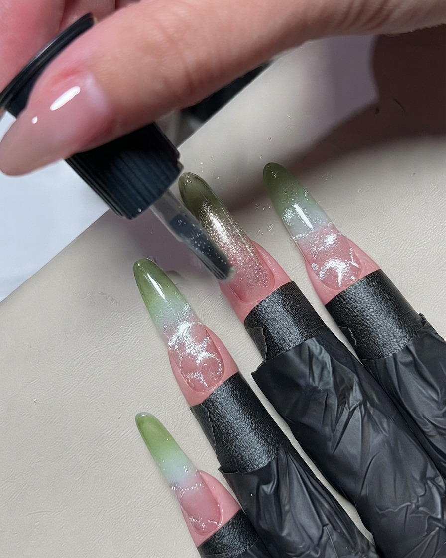 Un pequeño pincel para arte de uñas aplicando una línea fina de esmalte en gel metálico plateado por el centro de una uña ombre.