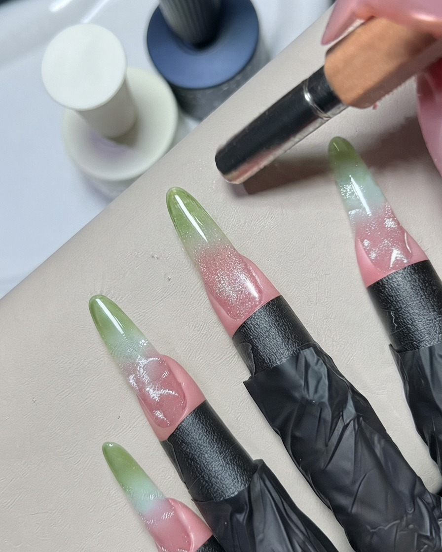 Una herramienta de punteado o detalle metálica difuminando los detalles de gel plateado en una uña decorada.