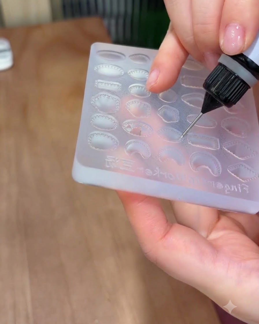 Una boquilla de precisión llenando una cavidad de gema ovalada en un molde de silicona con gel sólido transparente.
