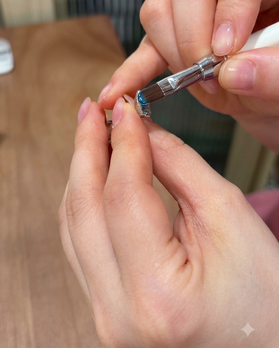 Un pincel para uñas aplicando un vibrante gel de ojo de gato azul sobre la superficie superior de una gema moldeada en 3D.
