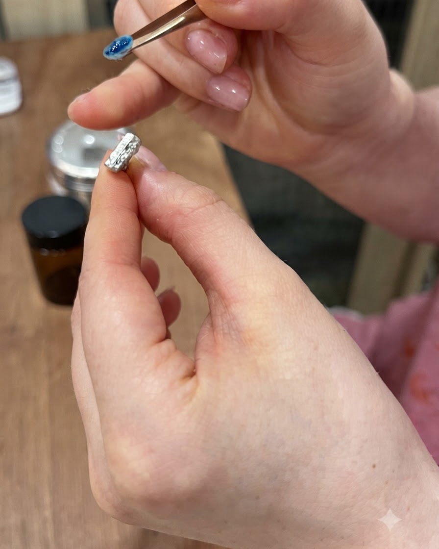 Un primer plano de pinzas de precisión levantando una pequeña gema azul en 3D de un soporte magnético para uñas.
