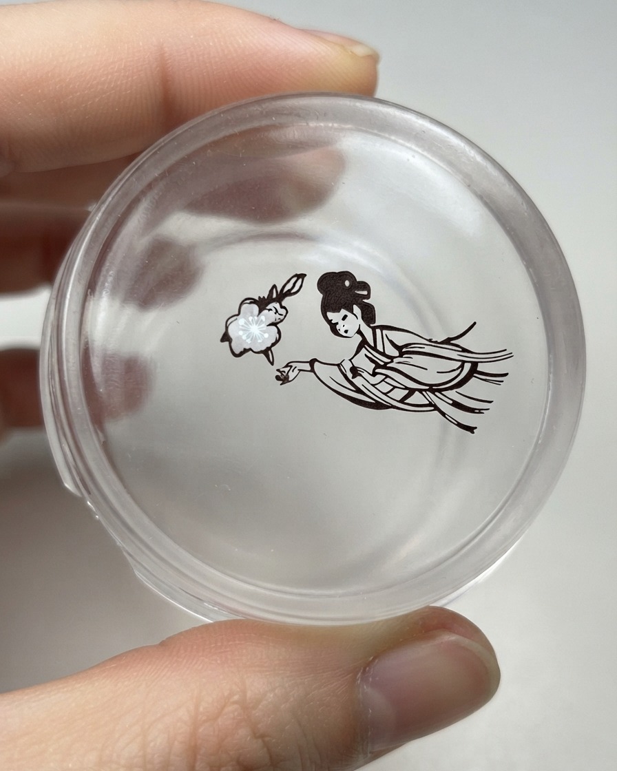 La cabeza de un sello de silicona transparente sosteniendo el diseño transferido de una flor junto a una figura femenina tradicional detallada.
