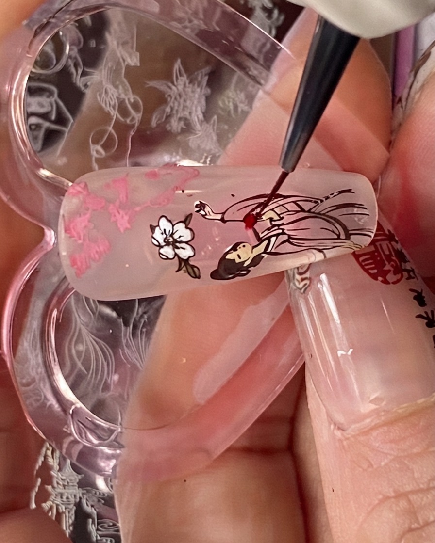 Un pincel de detalle aplicando líquido blooming rojo sobre la porción del vestido de la figura estampada en una punta de uña.