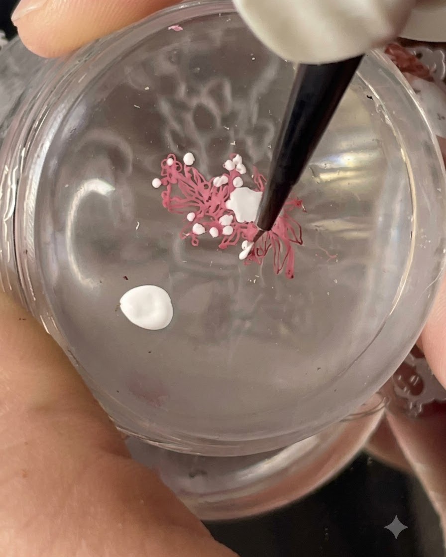 Un sello de silicona transparente sosteniendo un diseño de stamping floral transferido mientras se añaden puntos blancos con un pincel fino.