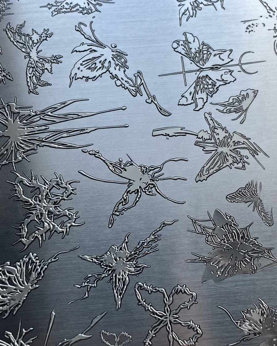 Una placa de estampación metálica con varios patrones complejos de mariposas y diseños abstractos.