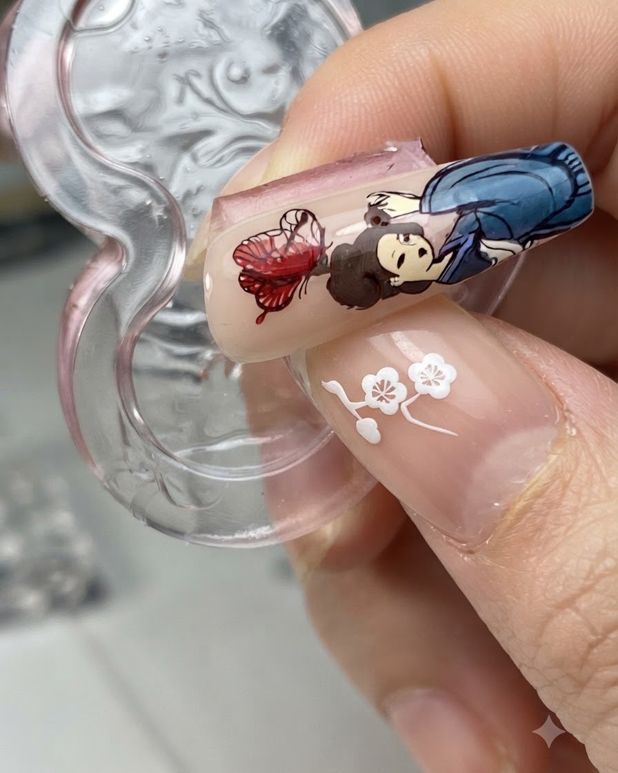 Una punta de uña con un diseño de mariposa transferido junto a un personaje de figura mientras se aplica líquido blooming.
