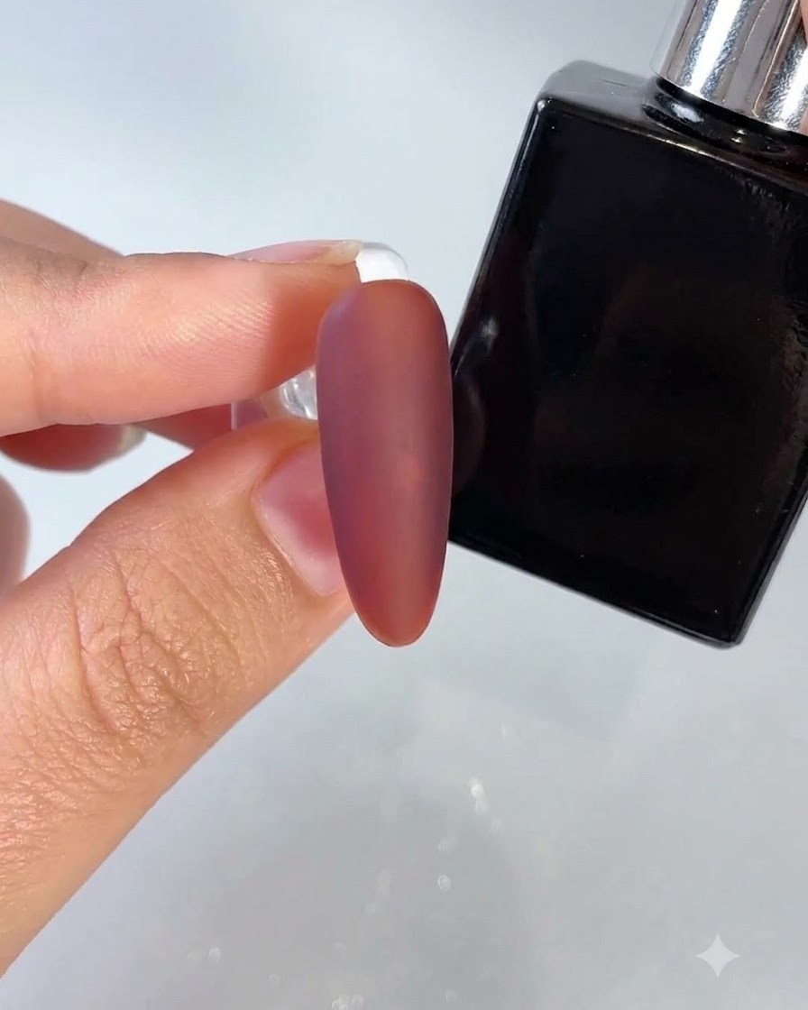 Una uña roja oscura con acabado mate siendo pintada con una botella de capa superior especializada cerca.