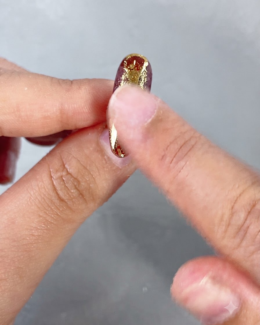Un dedo frotando polvo metálico dorado sobre elementos decorativos elevados en una uña.