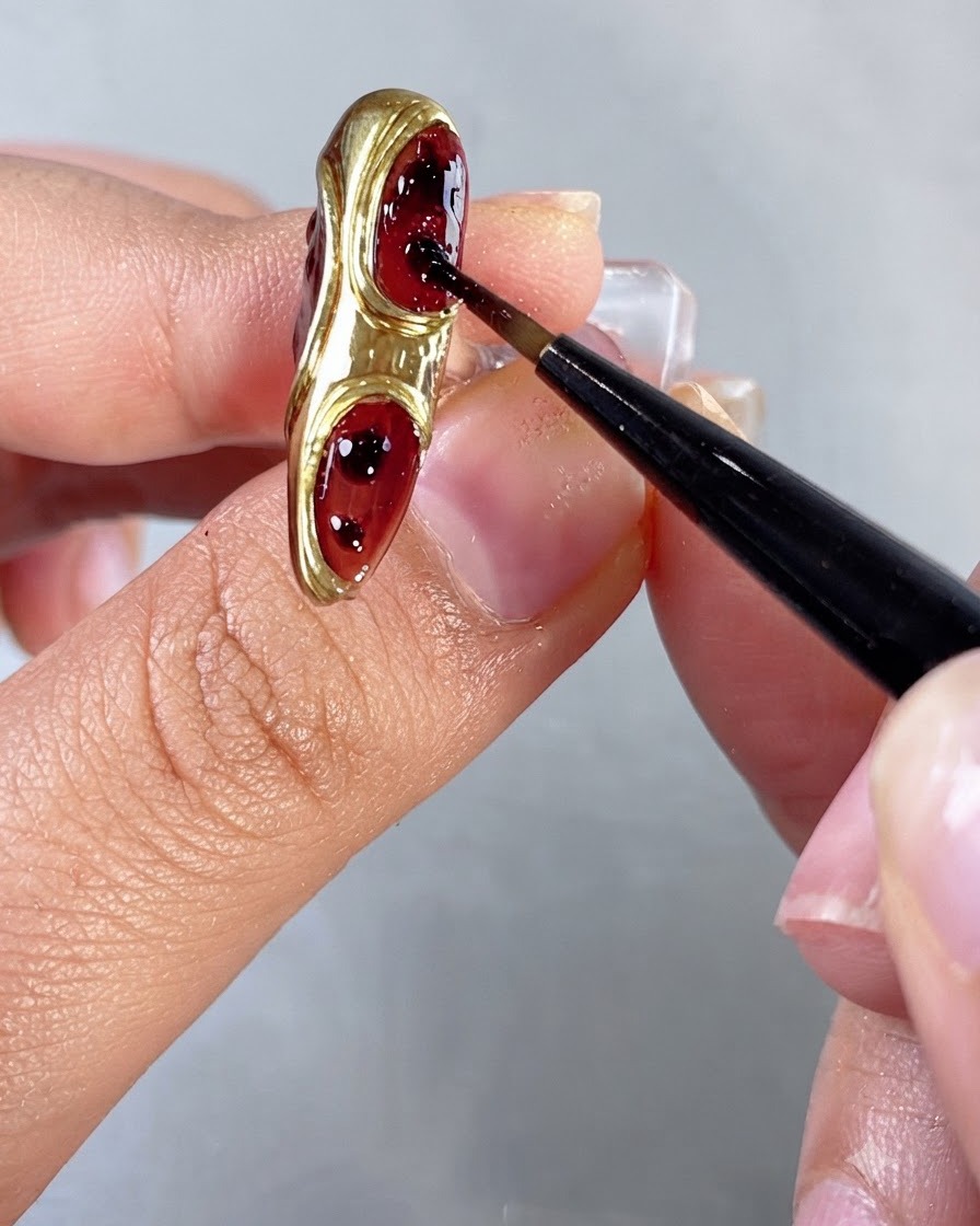 Un pincel difuminando y esparciendo pequeños puntos de gel rojo dentro de los espacios rebajados de las uñas.