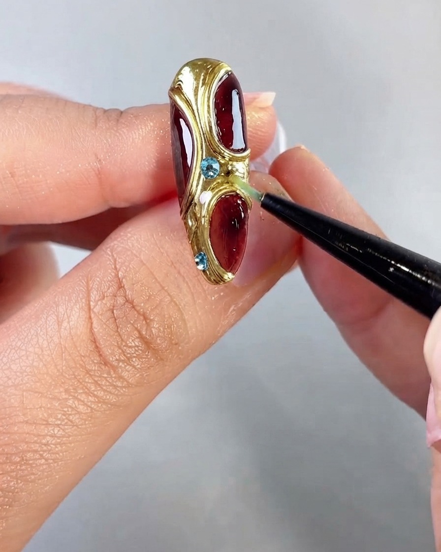 Pinzas colocando pequeños diamantes de imitación azules en las secciones con bordes dorados texturizados del arte de uñas.