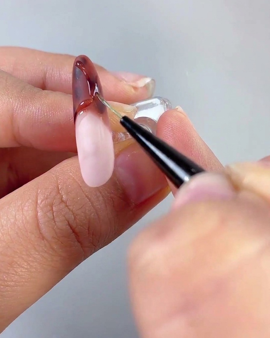 Un pincel aplicando una capa de capa superior sobre una base de uña rosa lechosa curada como parte de un tutorial de múltiples uñas.